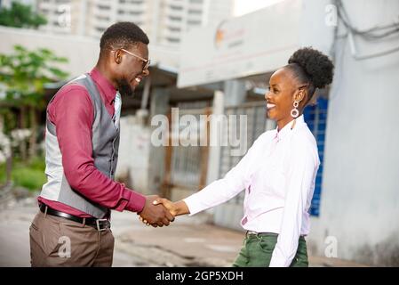 side view portrait of two businessmen, man and woman meeting on the street and shaking hands smiling in the street Stock Photo
