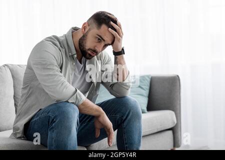 Man sit alone feeling sad worry regret or fear, depressed and desperate in sofa at home. Suffering emotional pain and unhappy, mental health. Young eu Stock Photo