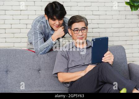 Asian senior businessman with digital tablet discuss together with young team in office. Father man and his son sit on sofa talking chatting on video Stock Photo