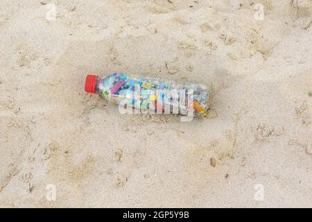 Bottle filled with microplastics collected from the sea lying on the sand of the beach Stock Photo