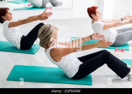 Group of middle aged women doing abdominal exercise in gym. Stock Photo