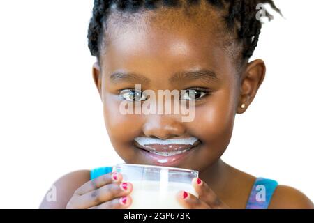 Close up face shot of sweet african girl with milk mustache.Girl holding glass of milk isolated on white background. Stock Photo