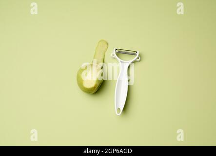 plastic knife for peeling vegetables and fruits and a green apple on a green background, top view Stock Photo