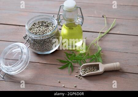 Hemp seeds in a wooden spoon, hemp oil and hemp stalks on a wooden table. Stock Photo
