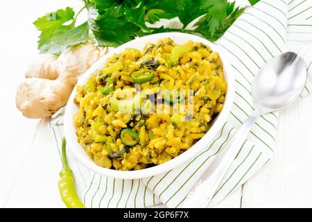 Indian national dish kichari made from mung bean, rice, stalk celery, spinach, hot pepper and spices in a bowl on a napkin, ginger on wooden board bac Stock Photo