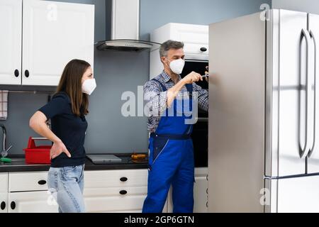 Fridge Repair Service. Refrigerator Repairman Technician In Face Mask Stock Photo