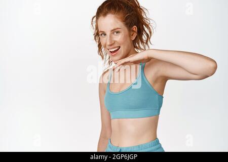 Young smiling sportswoman wiping sweat and looking satisfied with workout in gym, standing happy against white background Stock Photo