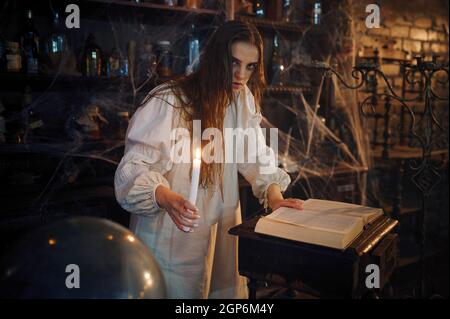 Young demonic woman with candle reads book of spells, demons casting out. Exorcism, mystery paranormal ritual, dark religion, night horror, potions on Stock Photo