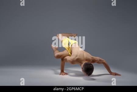 Muscular yoga stands on hands in difficult pose, meditation position, grey background. Strong man doing yogi exercise, asana training Stock Photo