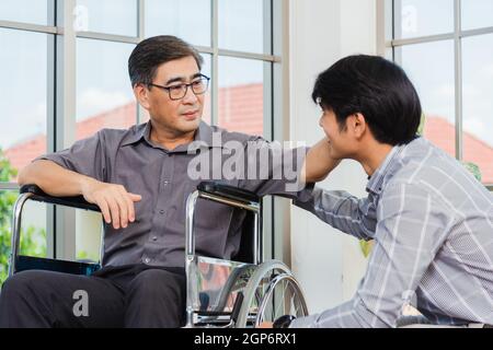 Asian senior disabled businessman in wheelchair discuss interacting together with the team in the office. The old man in a wheelchair and his young so Stock Photo
