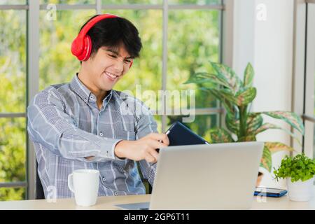 Asian young business man with red headphones he sitting on desk workplace using digital tablet play racing online video games, confident handsome man Stock Photo