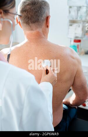 Doctor using stethoscope to check lung function on back of man Stock Photo