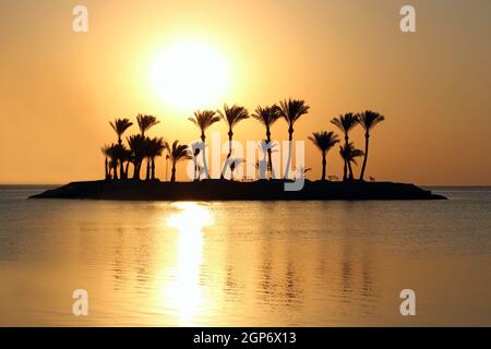 Beautiful place for privacy. Sunset over island in sea. Bright sun during dawn over the sea. Island with palm trees and benches in ocean. Summer vacat Stock Photo