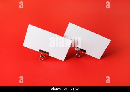 Two blank business cards and metal binder clips on red paper background. Stock Photo