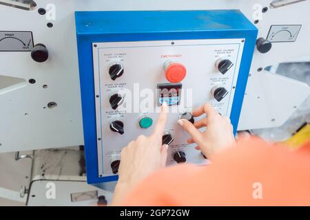 Woman pressing start button on label printing machine in print shop Stock Photo