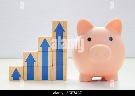 A piggy bank with wood blocks stacking as step stair with blue arrows up. Concept: Successful business, Business growth, Savings growth, Interest rate Stock Photo