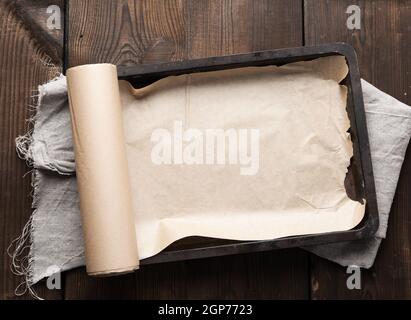 empty rectangular metal pan covered with brown parchment paper and paper rolls on a wooden table, top view Stock Photo