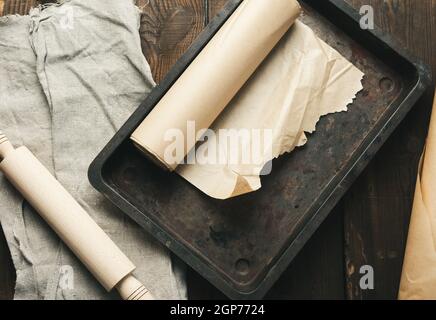 empty rectangular metal pan covered with brown parchment paper and paper rolls on a wooden table, top view Stock Photo