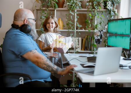 Smiling little daughter presents gift to bearded dad sitting at table in home office Stock Photo