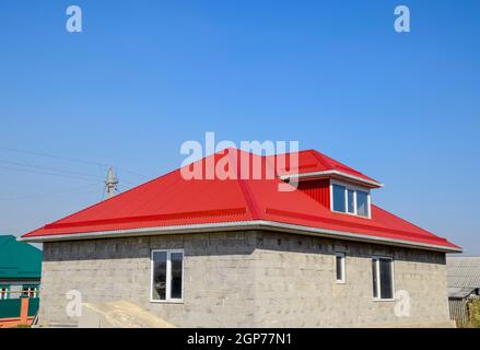 Red corrugated roof. House of cinder block. The house with plastic windows and a roof of corrugated sheet. Stock Photo
