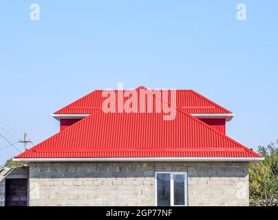 Red corrugated roof. House of cinder block. The house with plastic windows and a roof of corrugated sheet. Stock Photo