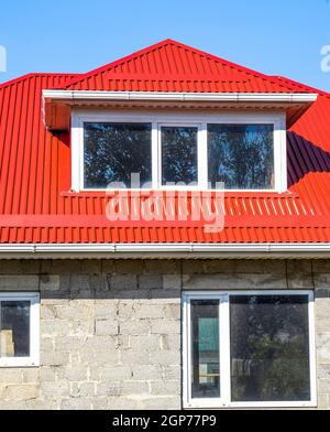 House with plastic windows and a red roof of corrugated sheet. Roofing of metal profile wavy shape on the house with plastic windows. House of cinder Stock Photo