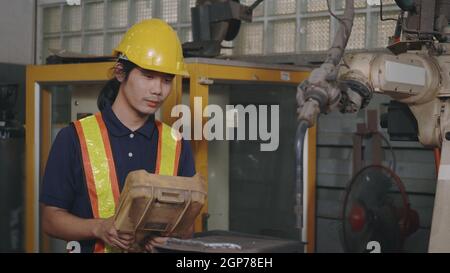 Asian engineering man check and control welding robotics automatic arms machine for automated programming indoors welding manufacturing industrial, Stock Photo