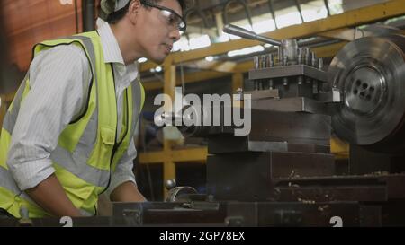 Asian professional mechanical engineer or operation man wear uniform goggles safety working on workshop metal lathe industrial manufacturing factory, Stock Photo