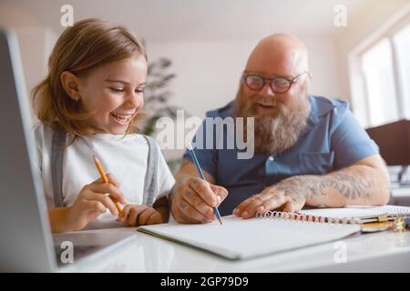Happy little schoolgirl and father helping her to do homework at table in room Stock Photo
