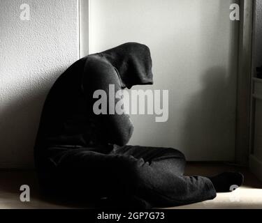 Depressed man sitting on the floor at home in front of a white background wall Stock Photo
