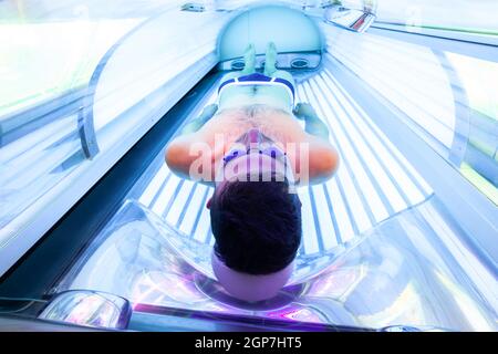 Young Thin Man At Solarium In Beauty Salon. Full tanning bed. Stock Photo