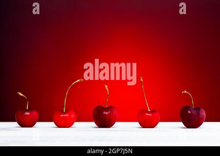 Row of freshly cherries on white wooden table over red background. Stock Photo
