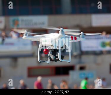 White drone quadcopter in flight with small camcorder. Stock Photo