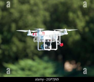 White drone quadcopter in flight with small camcorder. Stock Photo