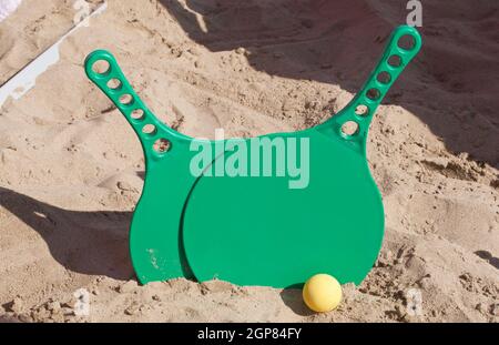 Two green rackets and a ball on the sandy beach. Stock Photo