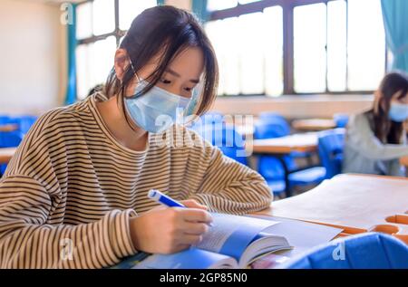 Teenager students wearing protection masks and studying in classroom Stock Photo