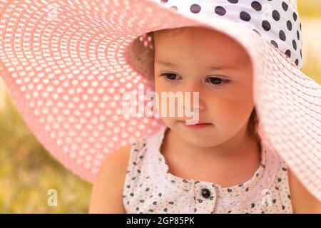 Face of a little cute girl 1-3 in a pink summer wide-brimmed hat in summer Stock Photo