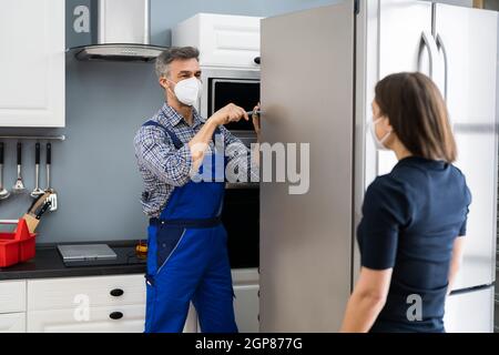 Fridge Repair Service. Refrigerator Repairman Technician In Face Mask Stock Photo