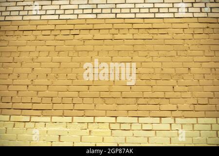 Brick wall painted with yellow paint. The texture of the wall of the building. Painted surface of the house. Stock Photo