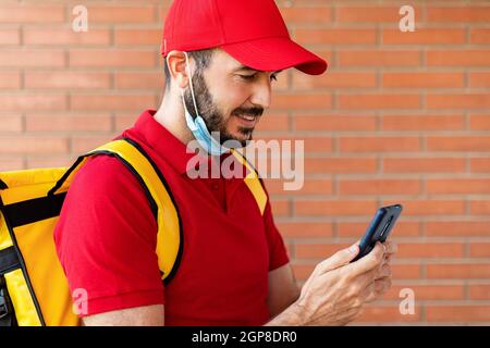 Delivery man in face mask using mobile phone while delivering packages Stock Photo