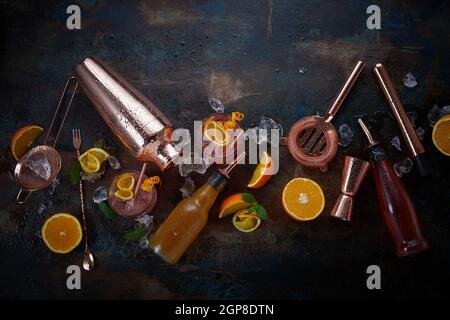 Cocktails or pub flat lay still life with copper bar equipment, chilled alcoholic beverages in glasses and sliced fresh oranges for garnishes scattere Stock Photo