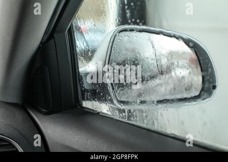 View from inside the car, looking at side mirror, wet from water and soap when being washed in carwash. Stock Photo