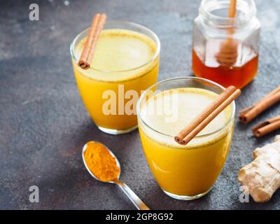 Healthy drink golden turmeric latte in glass.Gold milk with turmeric,ginger root,cinnamon sticks,turmeric powder and honey over black cement backgroun Stock Photo