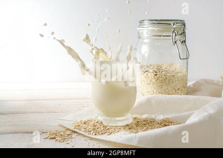 Vegan oat milk splash in a drinking glass and a storage jar on a light wooden table with a white napkin, healthy lactose free and non dairy alternativ Stock Photo