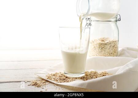 Vegan oat milk is poured into a drinking glass, healthy non dairy alternative on a light wooden table, copy space, selected focus, narrow depth of fie Stock Photo