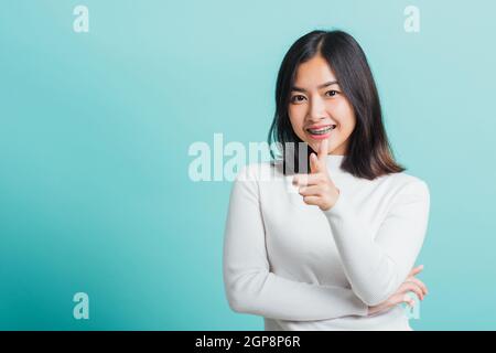 Young beautiful Asian woman smiling point finger at you with a confident expression, Portrait female pointing finger gesture towards you, studio shot