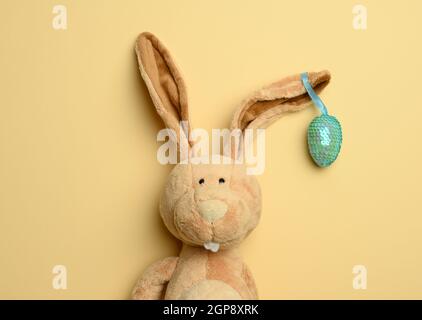 cute plush bunny with long ears, decorative egg hanging on the ear, easter background Stock Photo