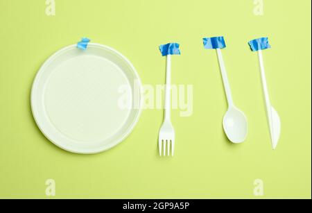 disposable plastic forks and spoons glued with blue tape on a green background, avoiding plastic, preserving the environment Stock Photo
