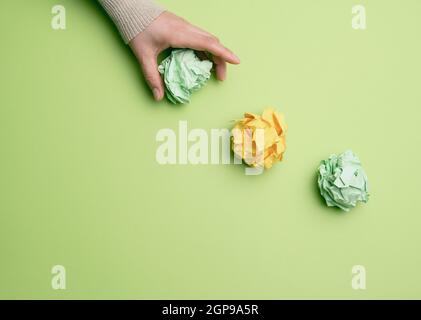 three crumpled balls of colored paper on a green background, hand throws paper Stock Photo