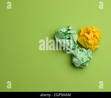 three crumpled balls of colored paper on a green background, copy space Stock Photo